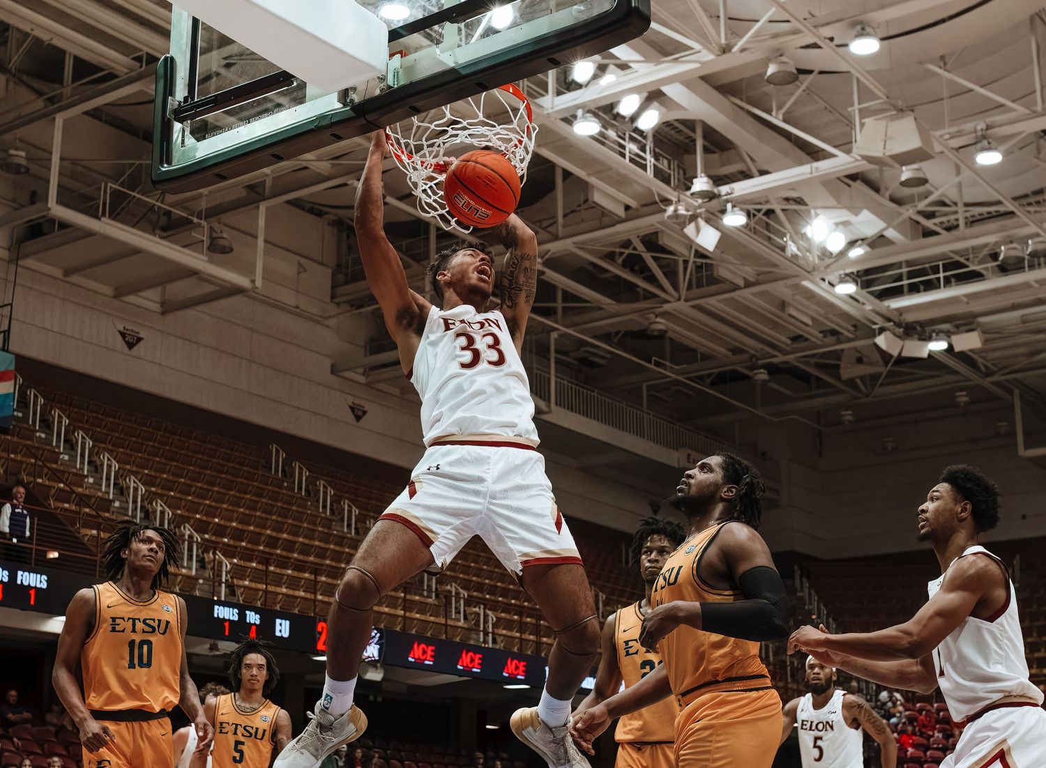 Basketball player in white jersey dunks the ball over defenders in orange uniforms.