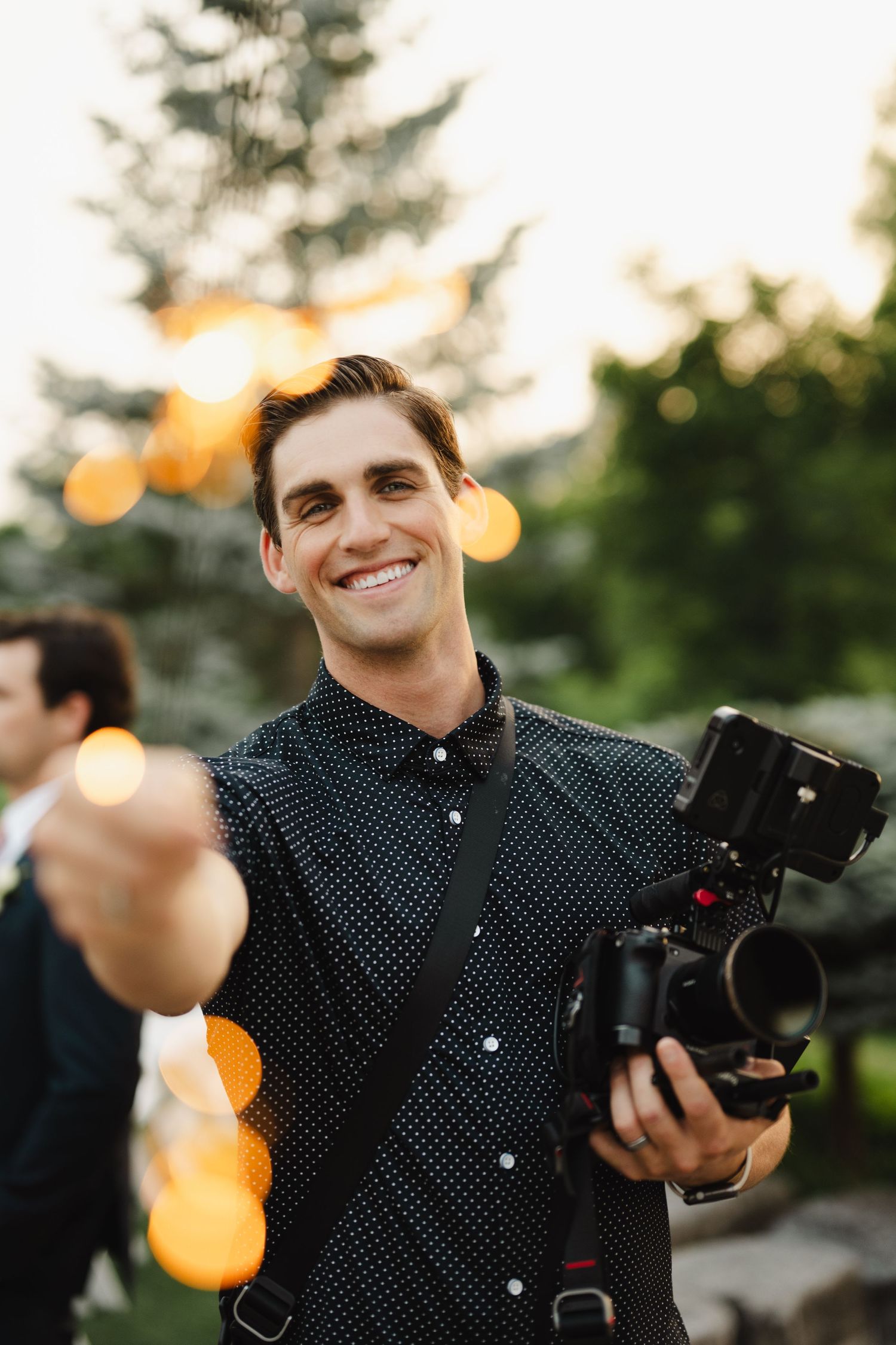 Professional photographer in polka dot shirt holding camera equipment during golden hour outdoor shoot.