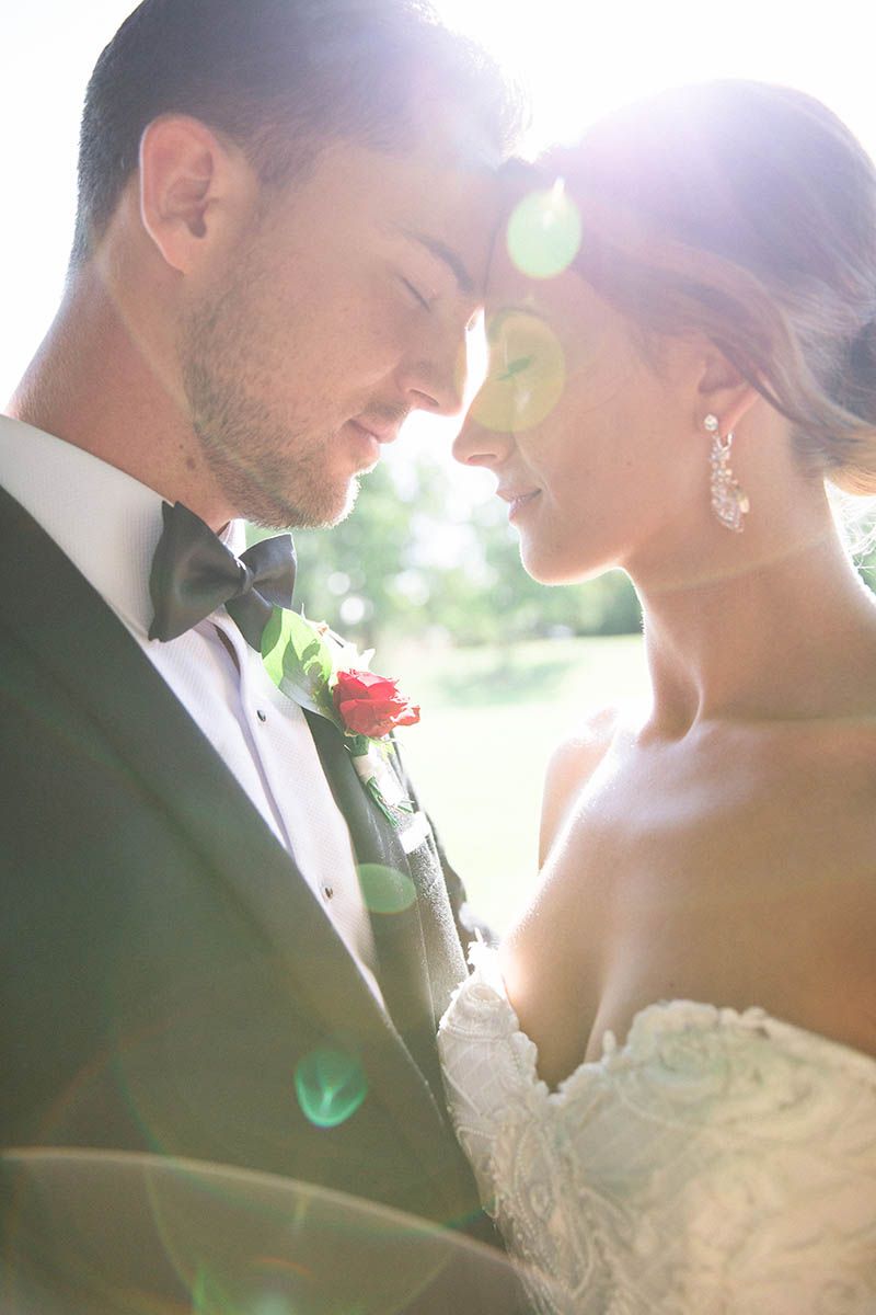 Romantic sunlit wedding portrait of couple in formal attire sharing an intimate moment outdoors.