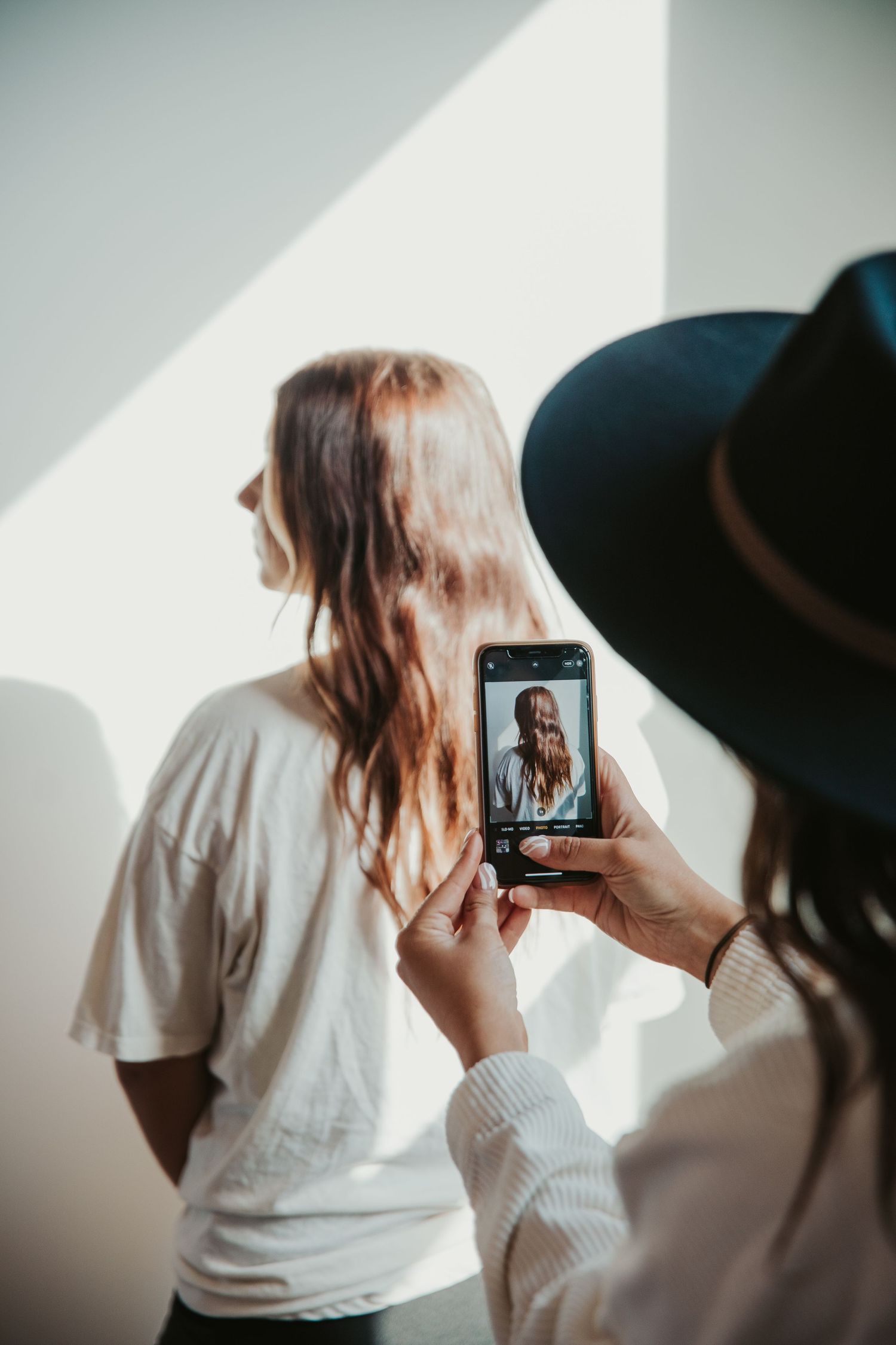 Behind-the-scenes photo shoot with photographer capturing model against white wall.