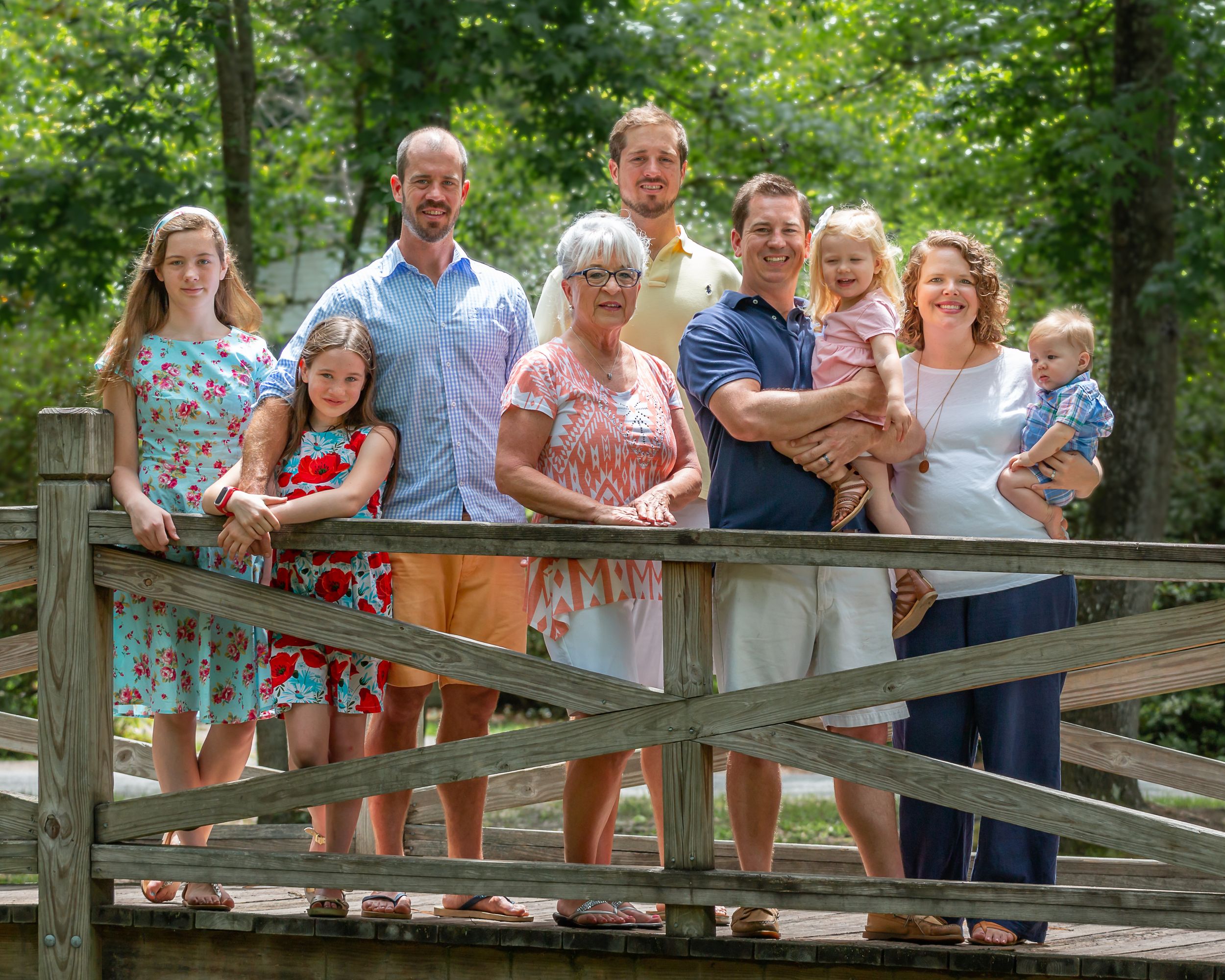 Extended family posing together on wooden bridge in outdoor nature setting.