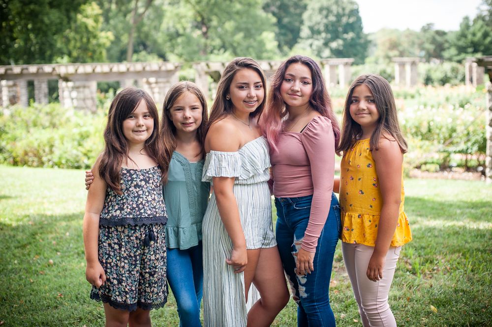 Group of friends in summer outfits pose together in a sunny garden setting.