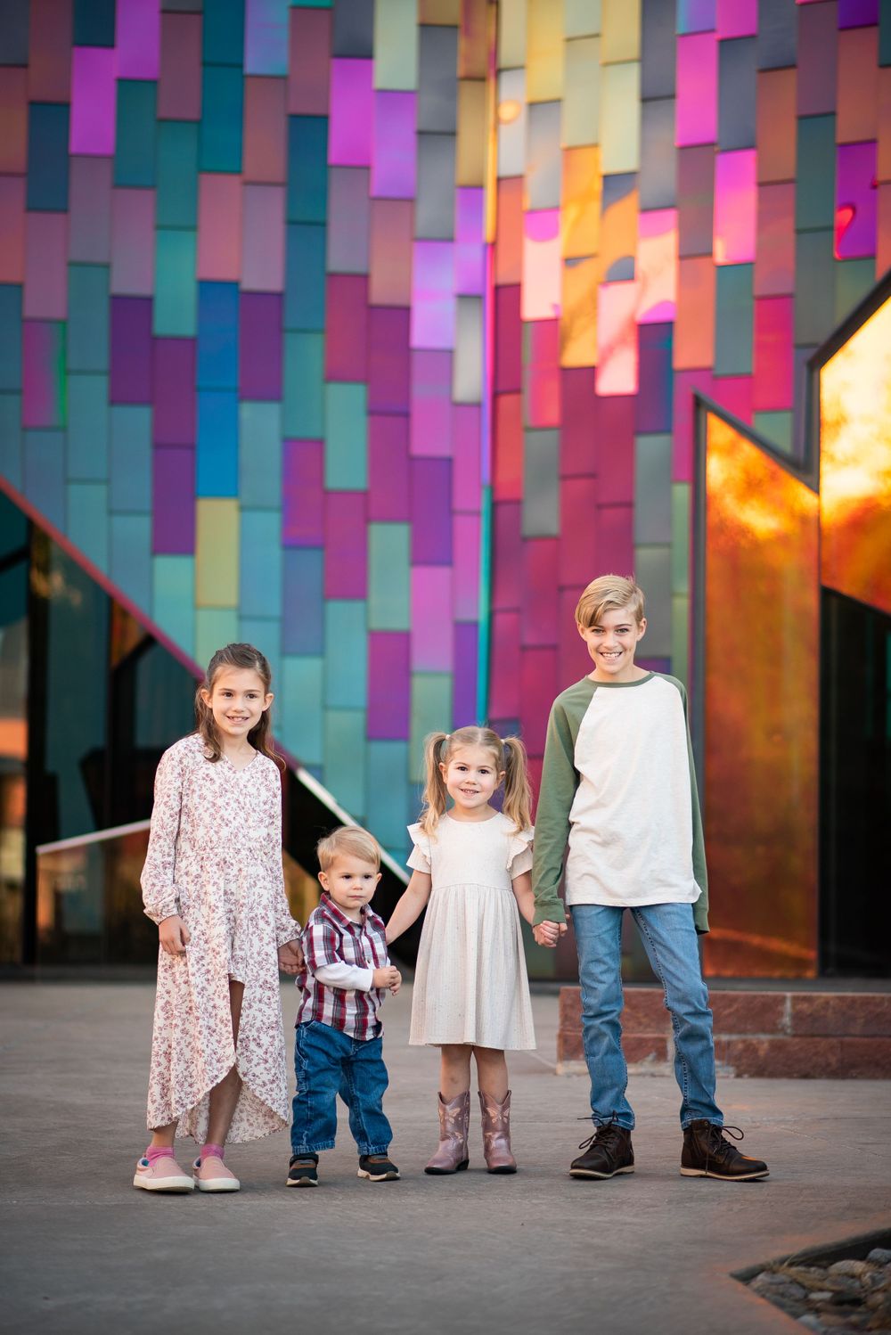 Four children stand together against a vibrant multicolored geometric wall background.