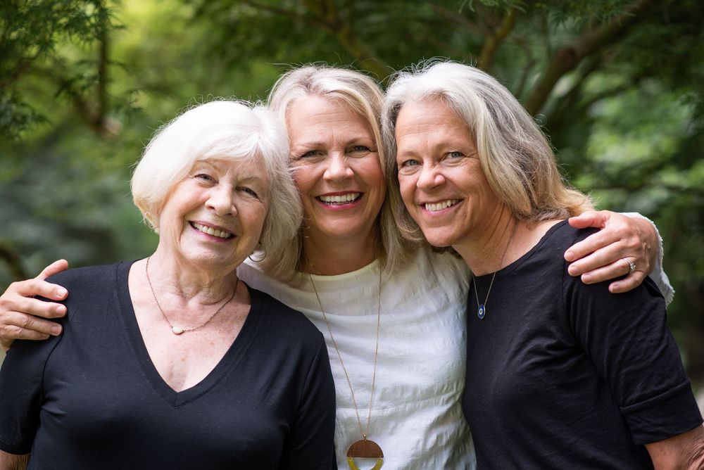 Three generations of women embrace and smile warmly together in an outdoor setting.