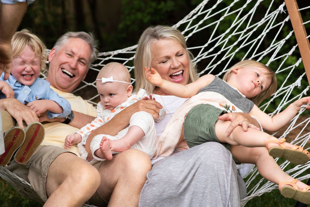 A happy family laughs together while relaxing in a hammock on a sunny day.