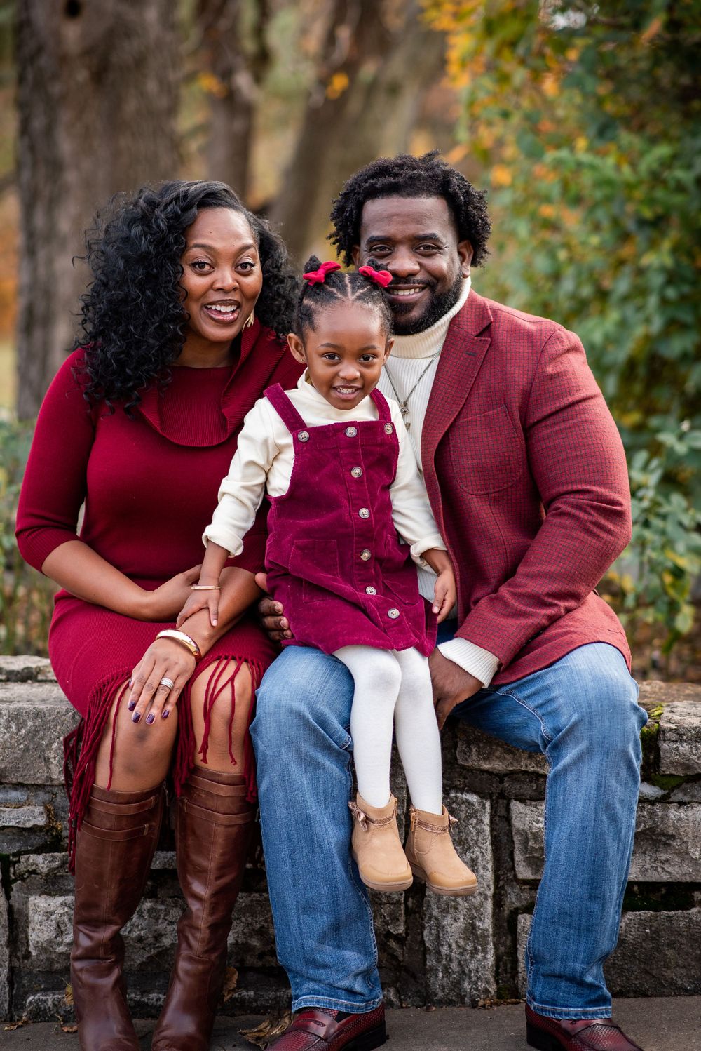 A family in coordinating burgundy outfits shares a joyful moment on a stone wall during fall.