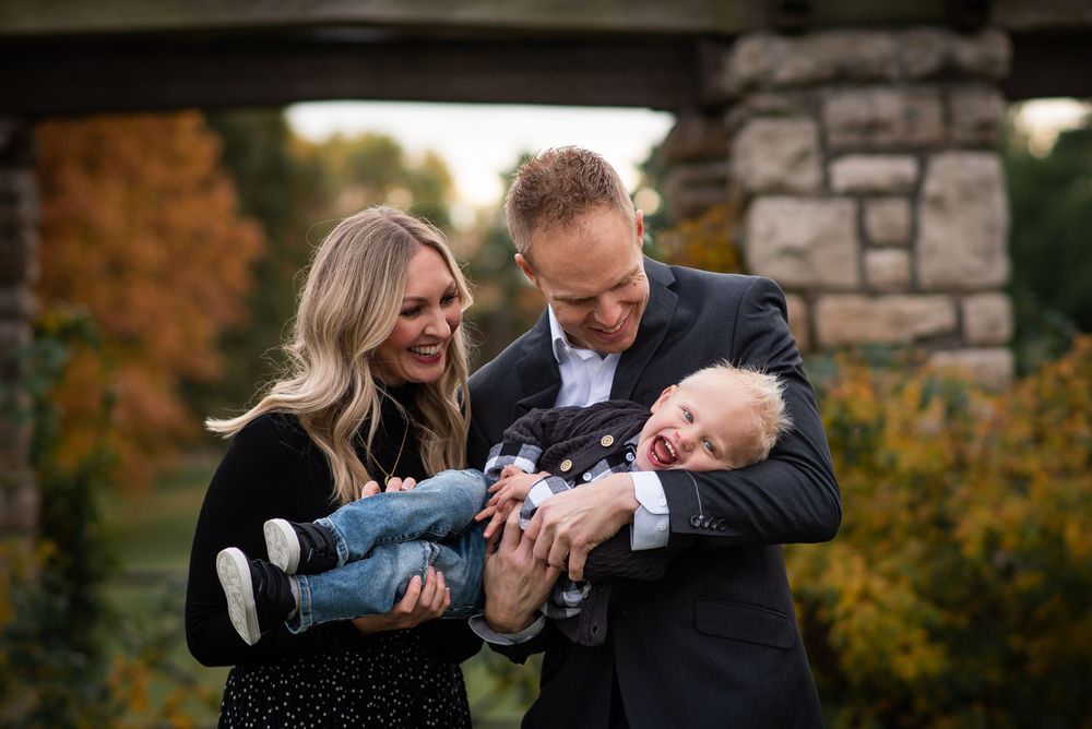Couple sharing a playful moment with a baby outdoors during an autumn photo session.
