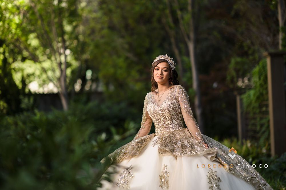 A model in an ornate champagne-colored ball gown poses in a garden setting.