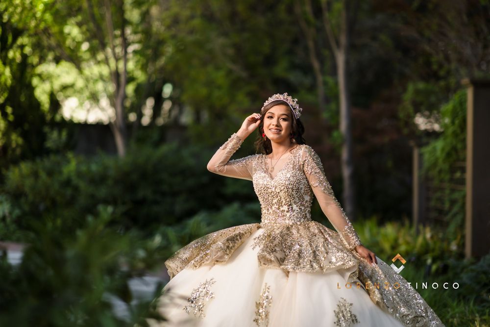 A model in a sparkly champagne ball gown poses gracefully in a garden.