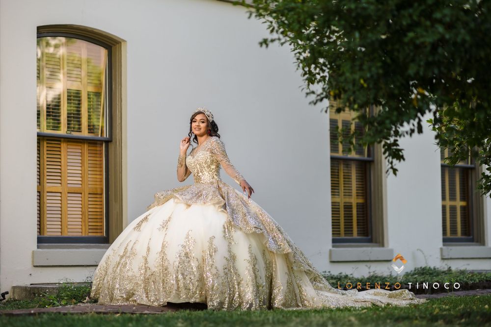 Elegant ballgown with gold embellishments photographed against white building with vintage windows.