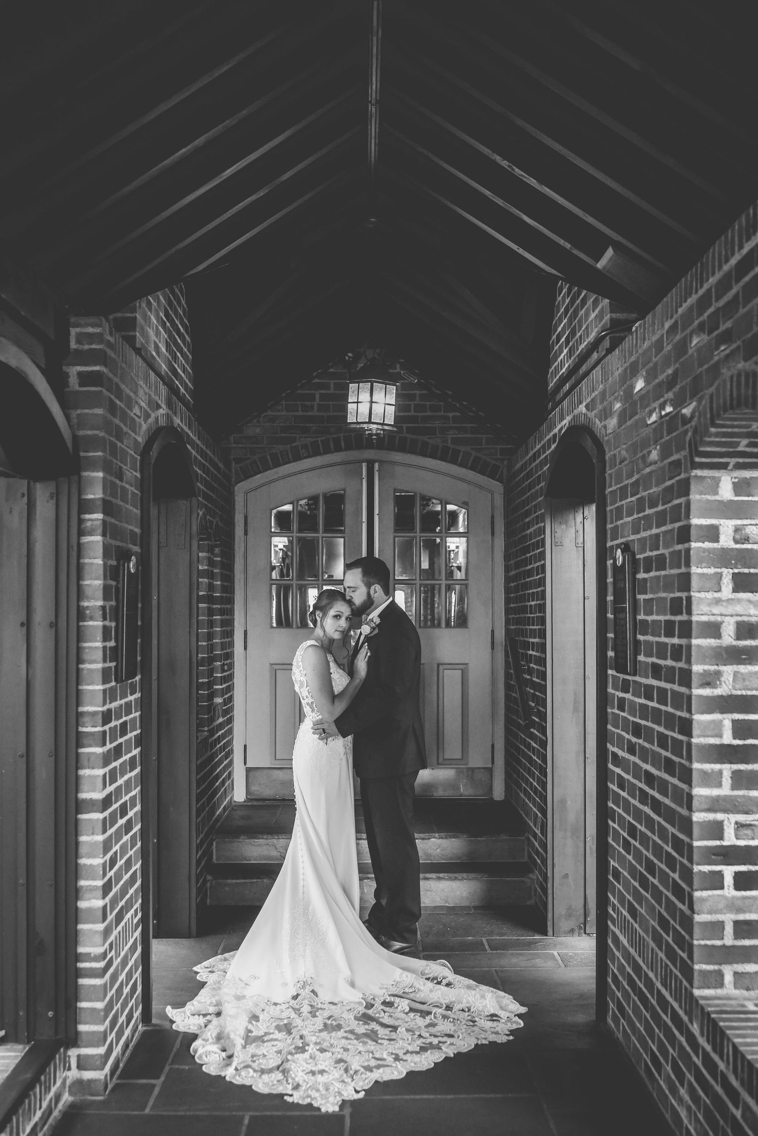 Dramatic wedding photography in brick corridor with elegant white gown and architectural details.