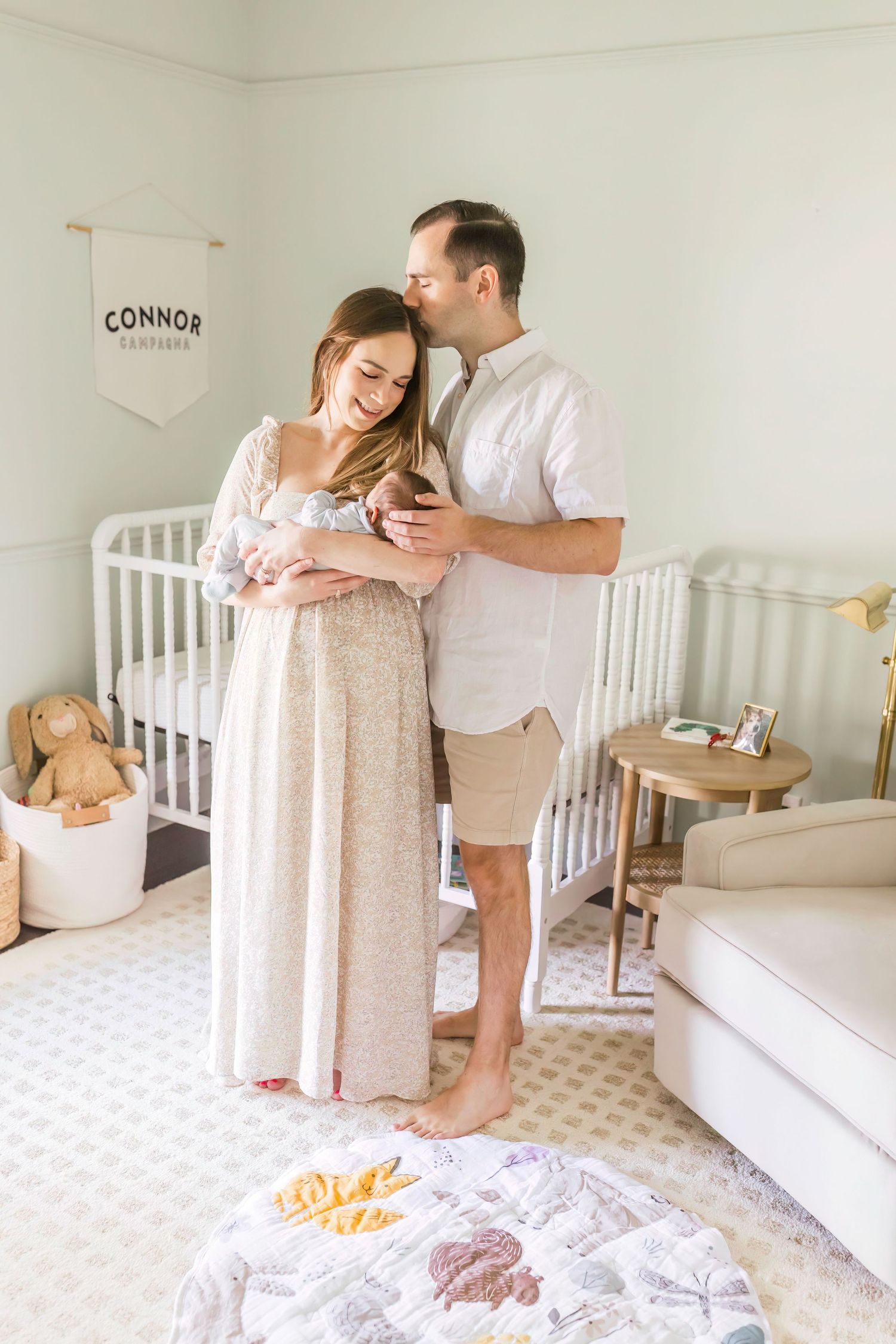 Tender moment between parents and newborn in neutral-toned nursery with white crib.