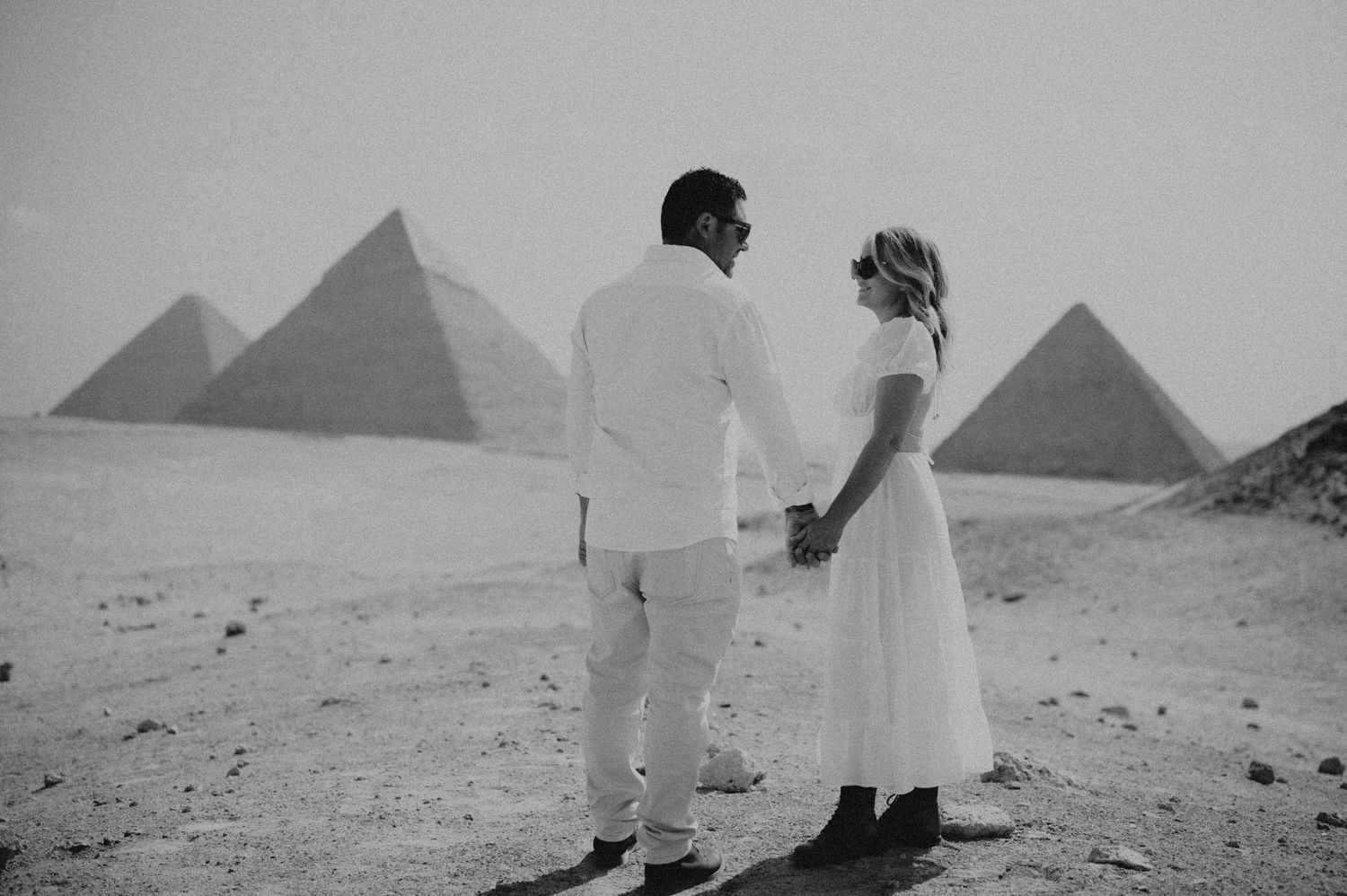 Black and white photograph of couple viewing pyramids together in Egyptian desert.
