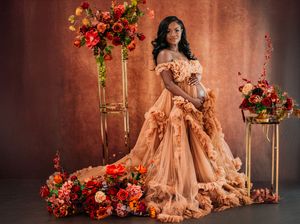 Elegant peach ballgown surrounded by floral arrangements with red and orange blooms against a rustic backdrop. Maternity
