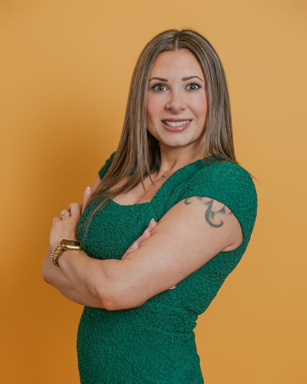Woman in emerald green top poses confidently against a warm orange background making a series of expressions.