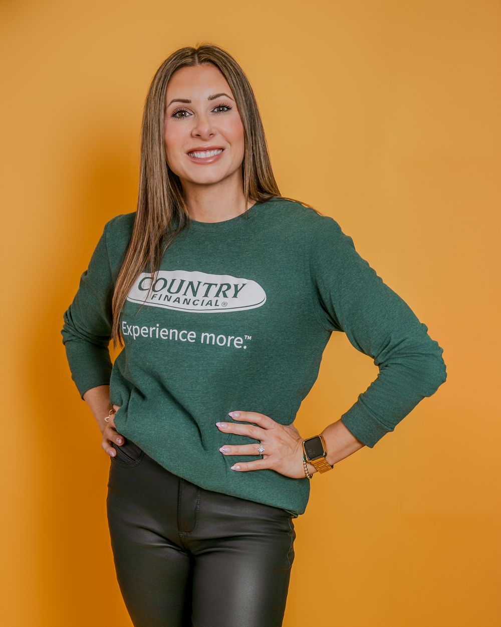 Woman in green sweatshirt and dark pants poses against orange background showing different casual modeling poses.