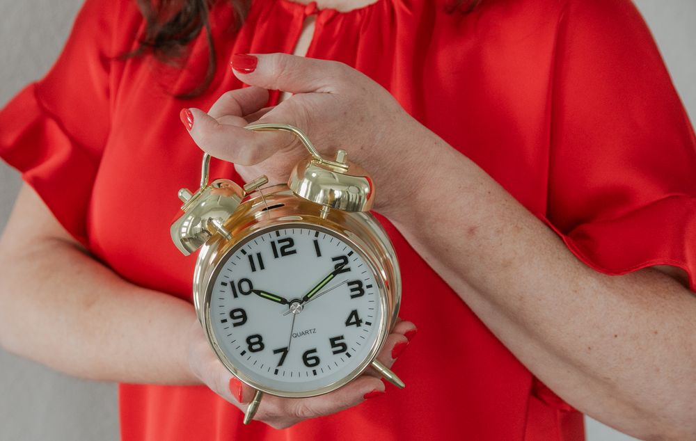 Hands holding a golden vintage alarm clock against a red blouse background. Denver Brand Photographer | Personal Branding