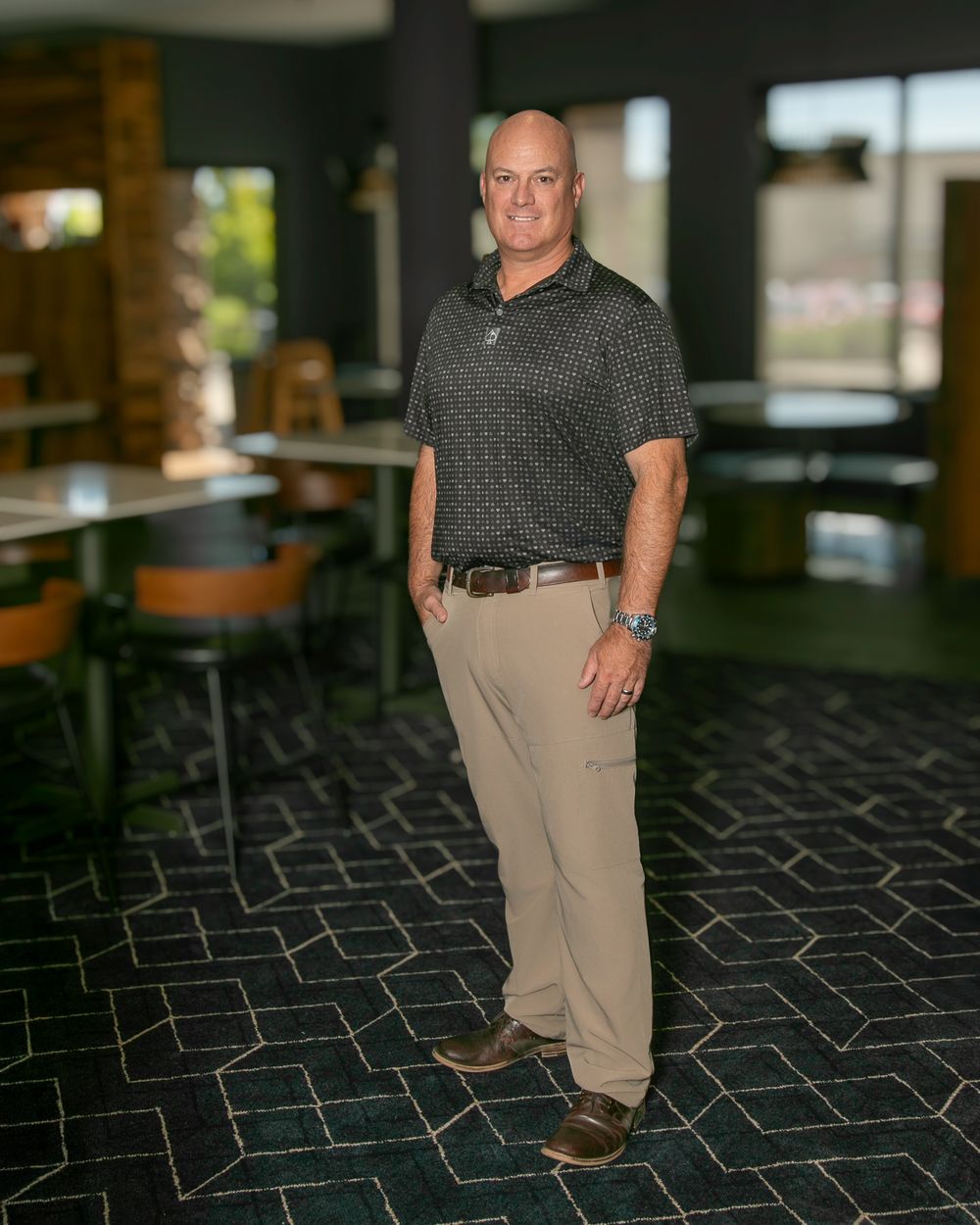 A person wearing a gray polo shirt and khaki pants stands on patterned carpet in an indoor office setting.