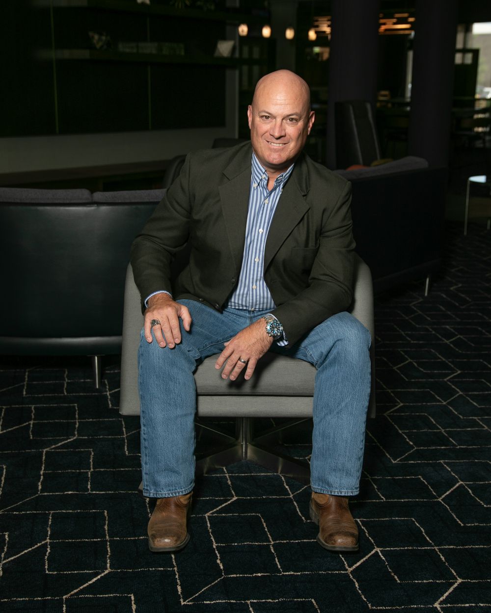 Professional portrait series of a businessman sitting on dark modern furniture against a black background.