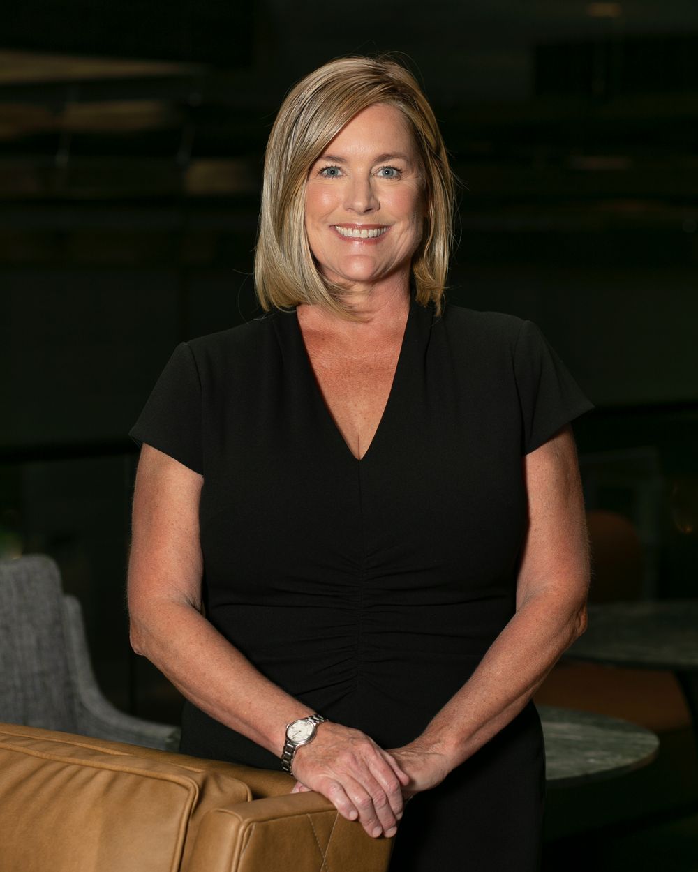 Professional headshot portrait of someone in a black top against a dark background with warm lighting.