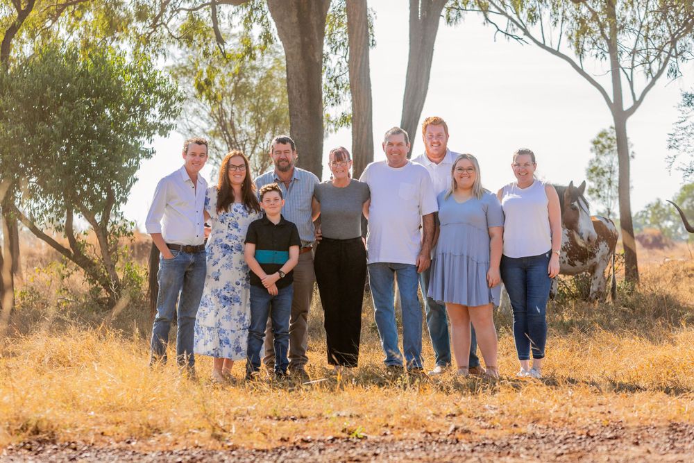 A family group poses outdoors in casual clothing against a backdrop of eucalyptus trees in natural sunlight.