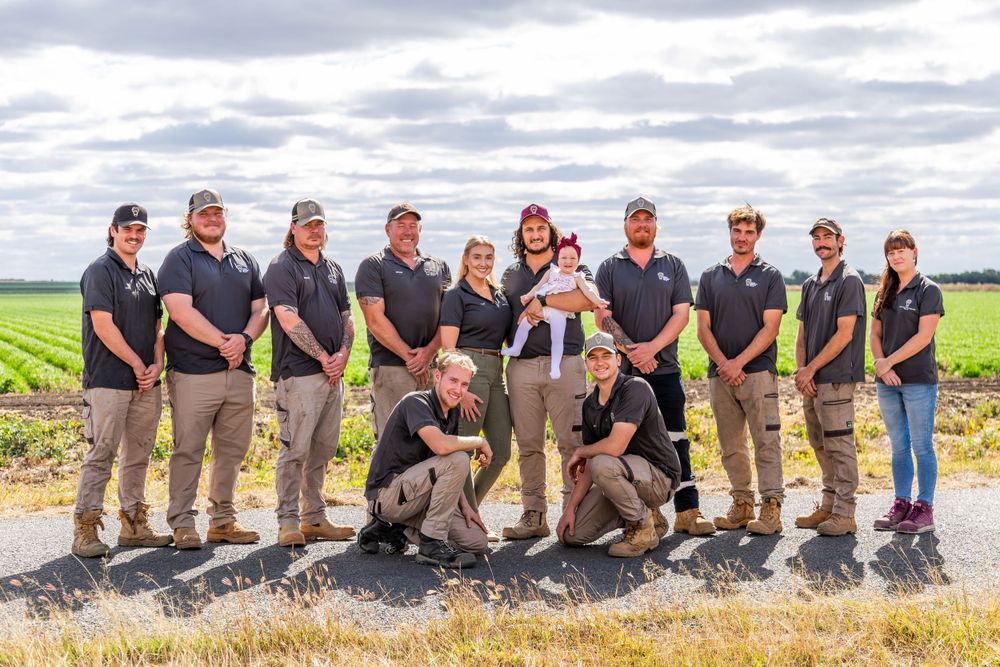 A team of professionals in matching black polos and khaki pants pose together on a grassy hill under cloudy skies.