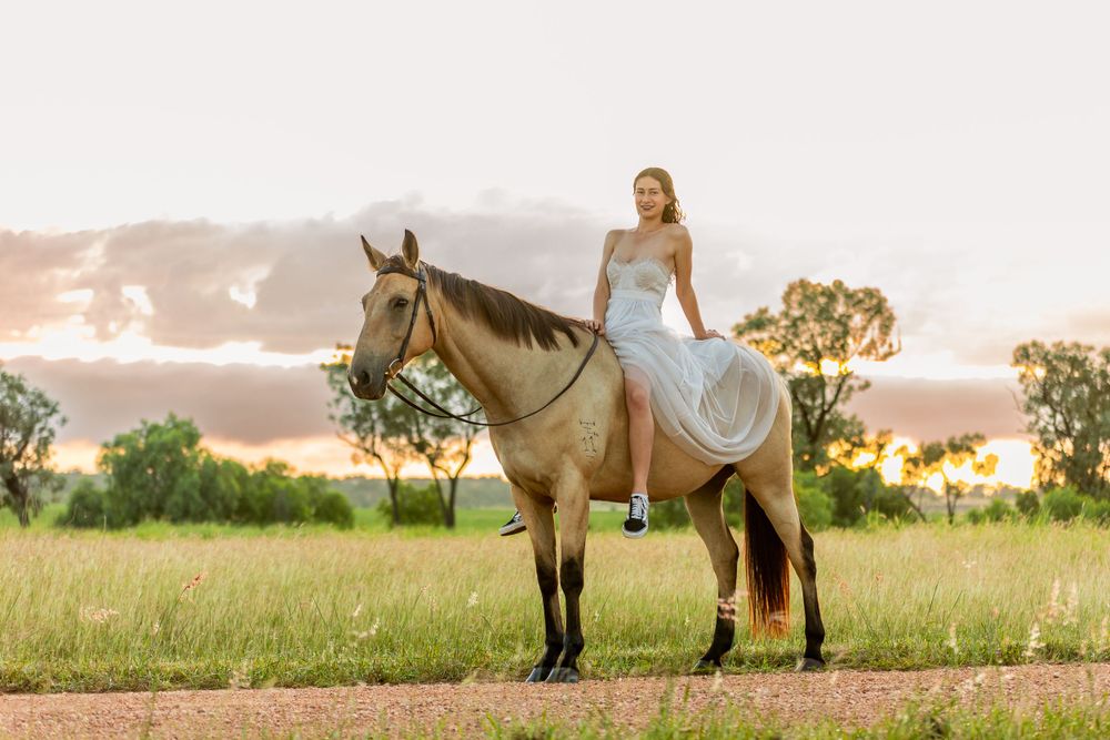 Person in white dress rides horseback during golden sunset in rural field.