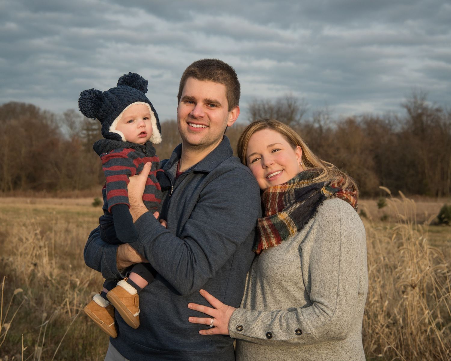 A family poses together in a field on an overcast day wearing cozy winter clothing.