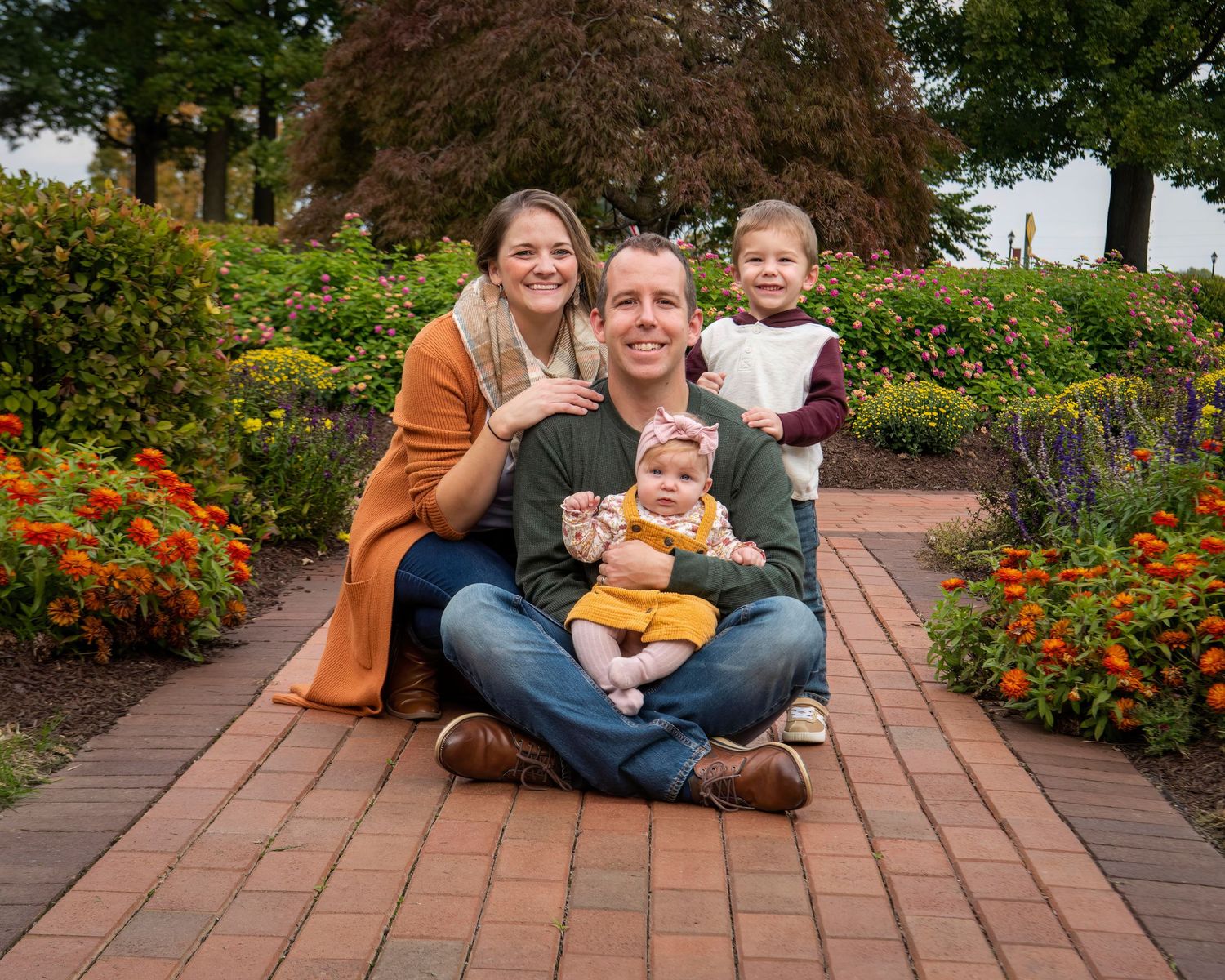 A family sits together on a brick pathway surrounded by vibrant orange flowers and lush garden landscaping.