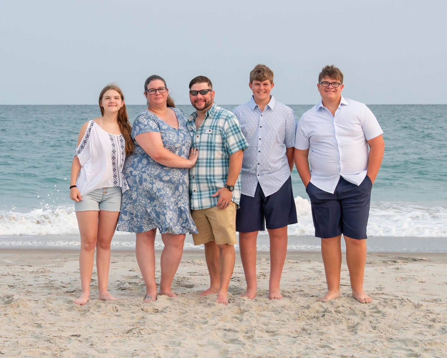 A group of five people standing together on a beach with the ocean waves in the background.