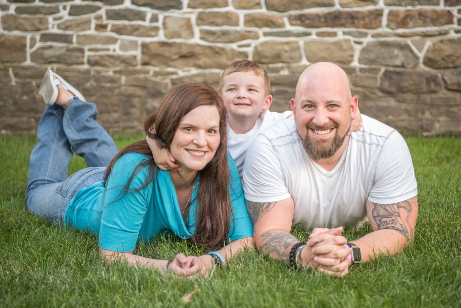 Family relaxing together on grass with stone wall background in outdoor portrait session.
