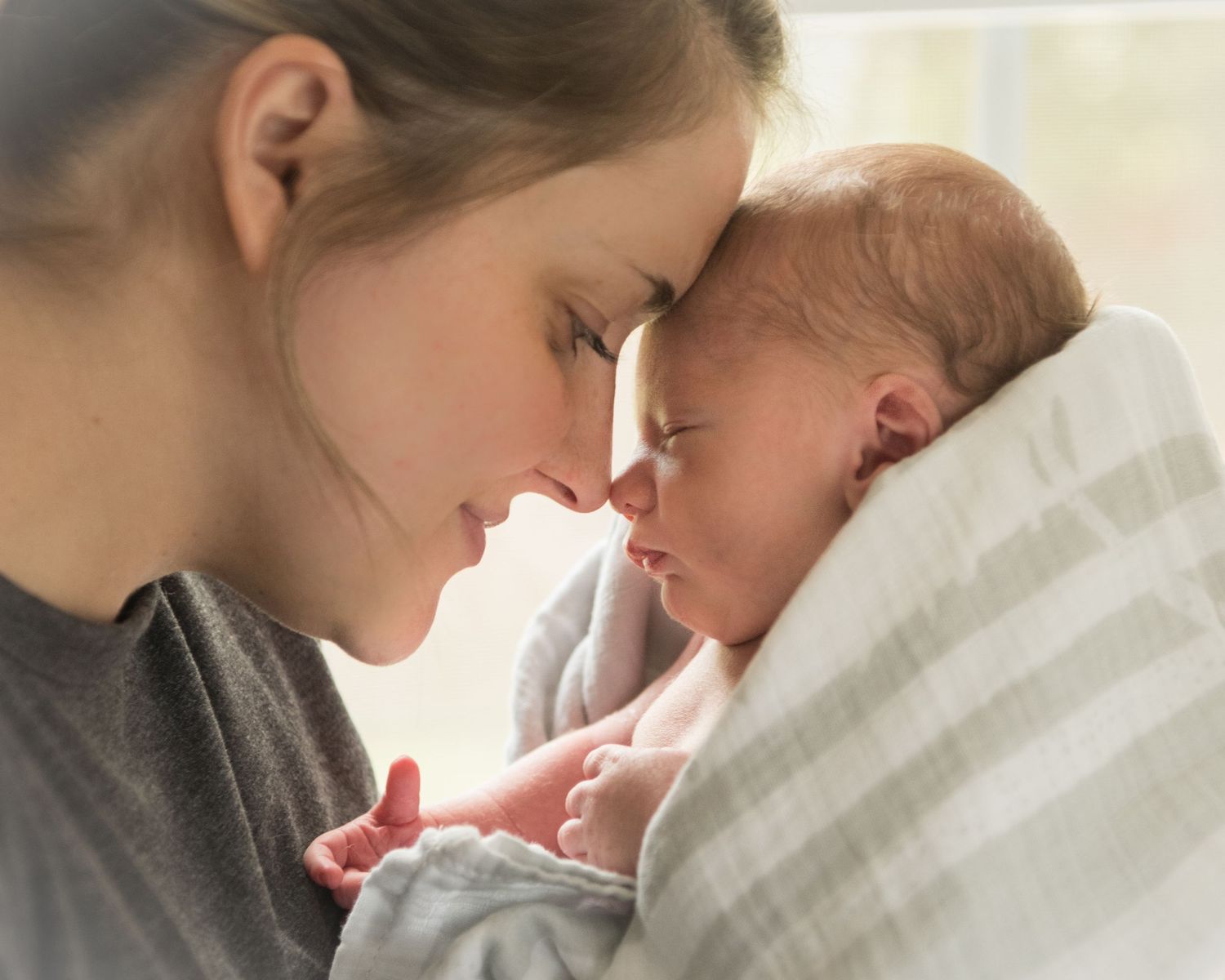 A tender moment between mother and newborn baby as they share a gentle nose touch while wrapped in soft white blankets.