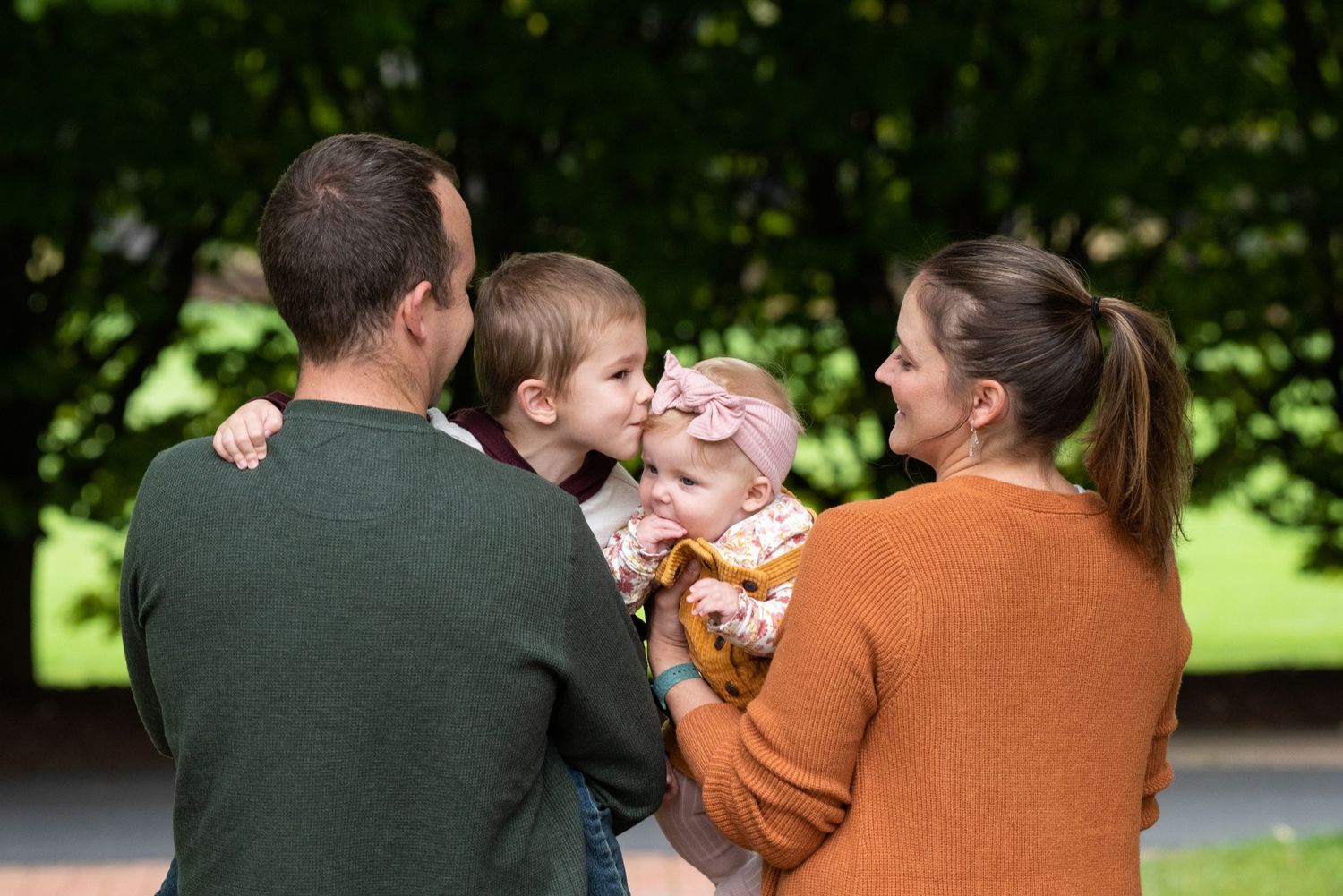 A family enjoys a tender moment together outdoors, wearing cozy sweaters on a sunny fall day.