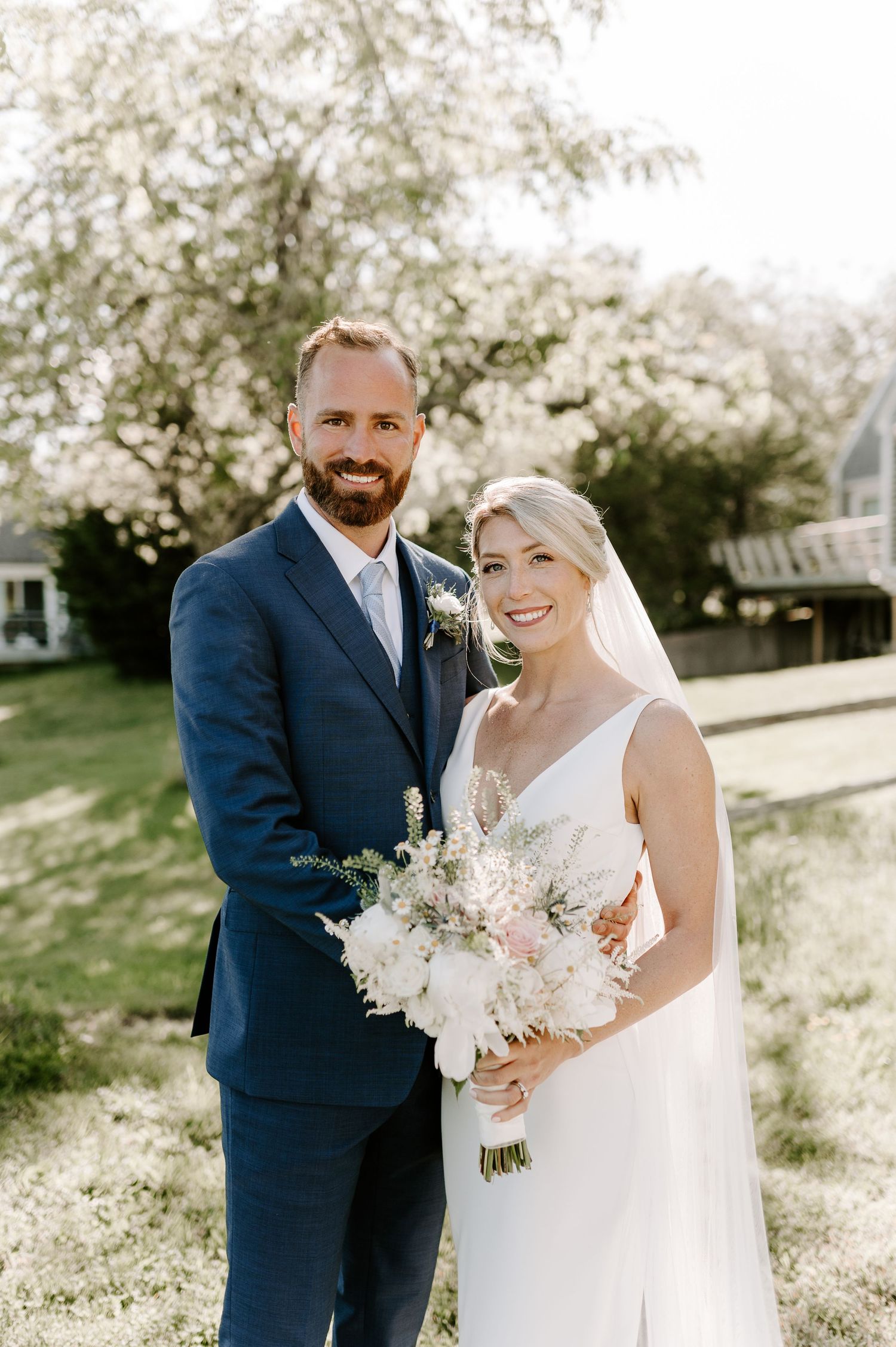 Romantic wedding portraits in sunlit garden with delicate bouquet and flowing dress.