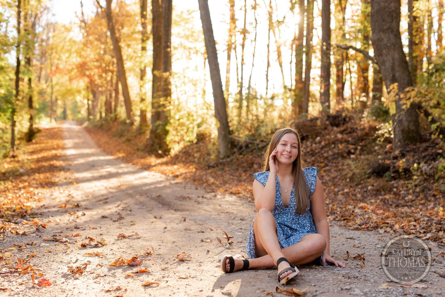 A blue dress on a wooded trail during golden hour with fall foliage in the background.