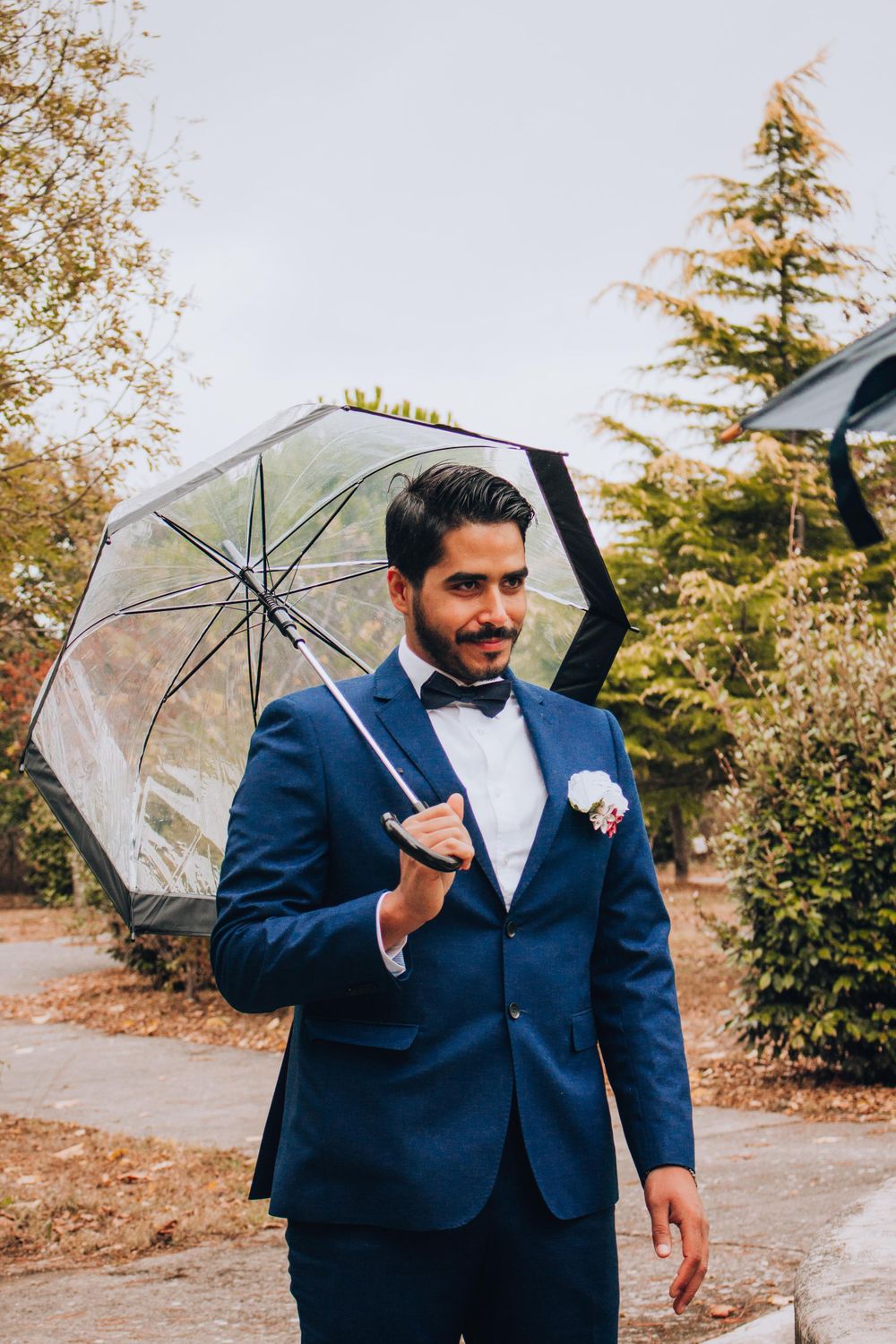 Groom walking with clear umbrella against autumn foliage background.