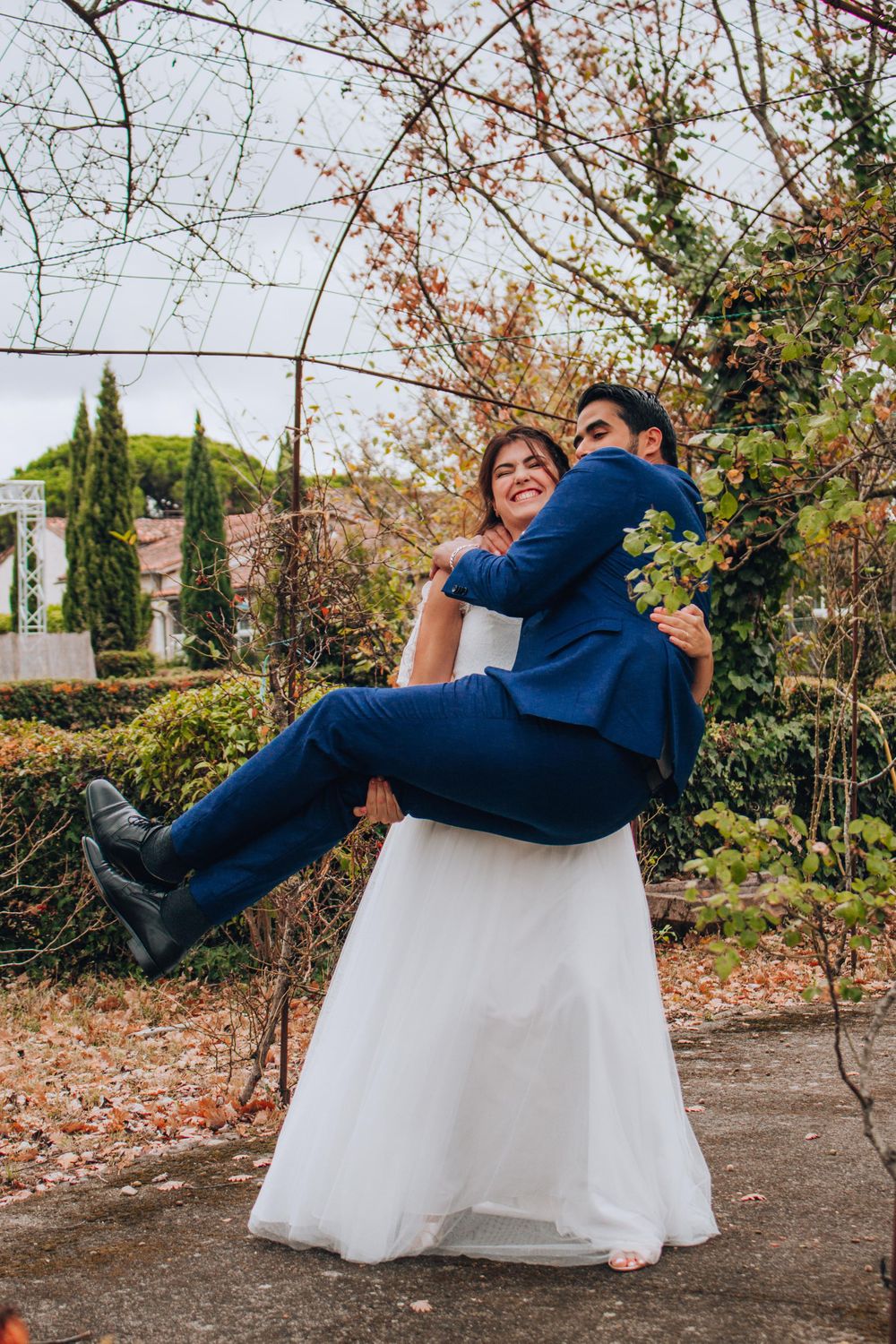 Playful wedding photo of bride lifting groom in garden setting.