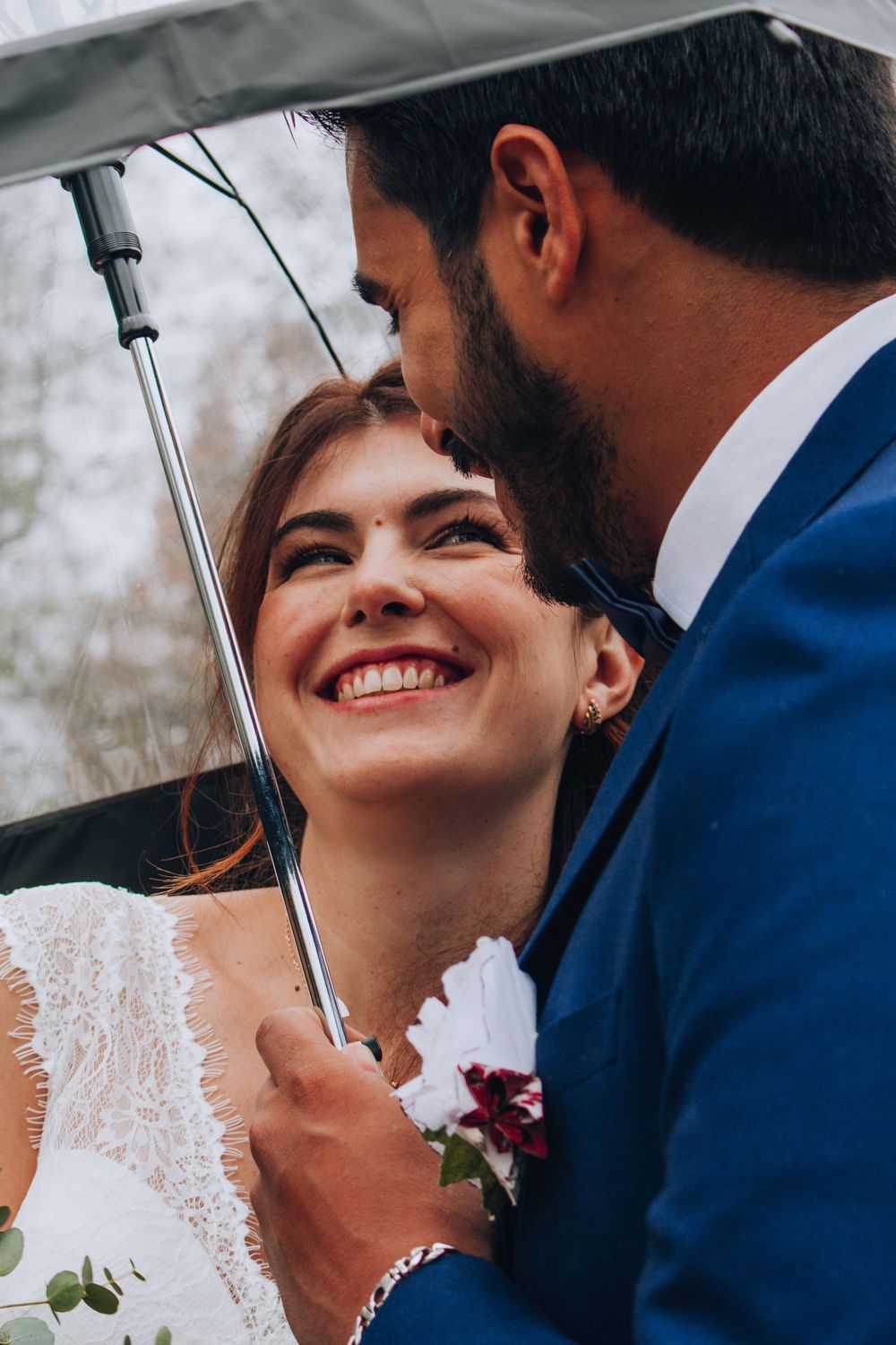 Romantic moment shared under a clear umbrella during outdoor wedding photoshoot.