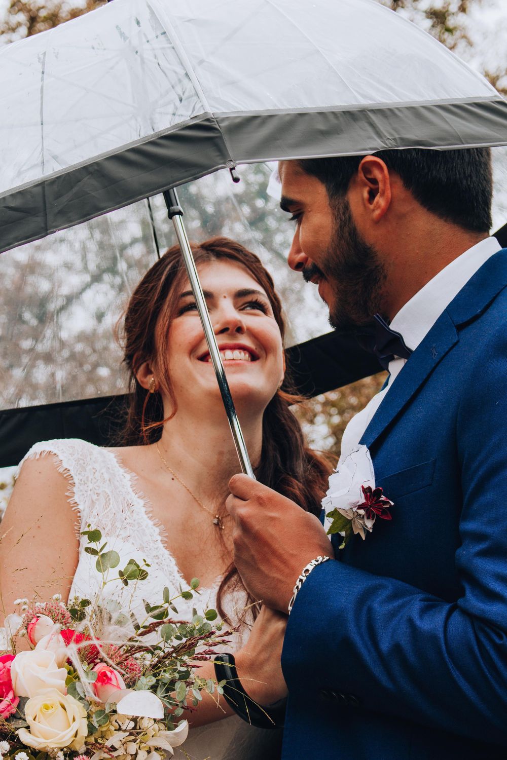 Joyful wedding couple sharing a tender moment under a clear umbrella.