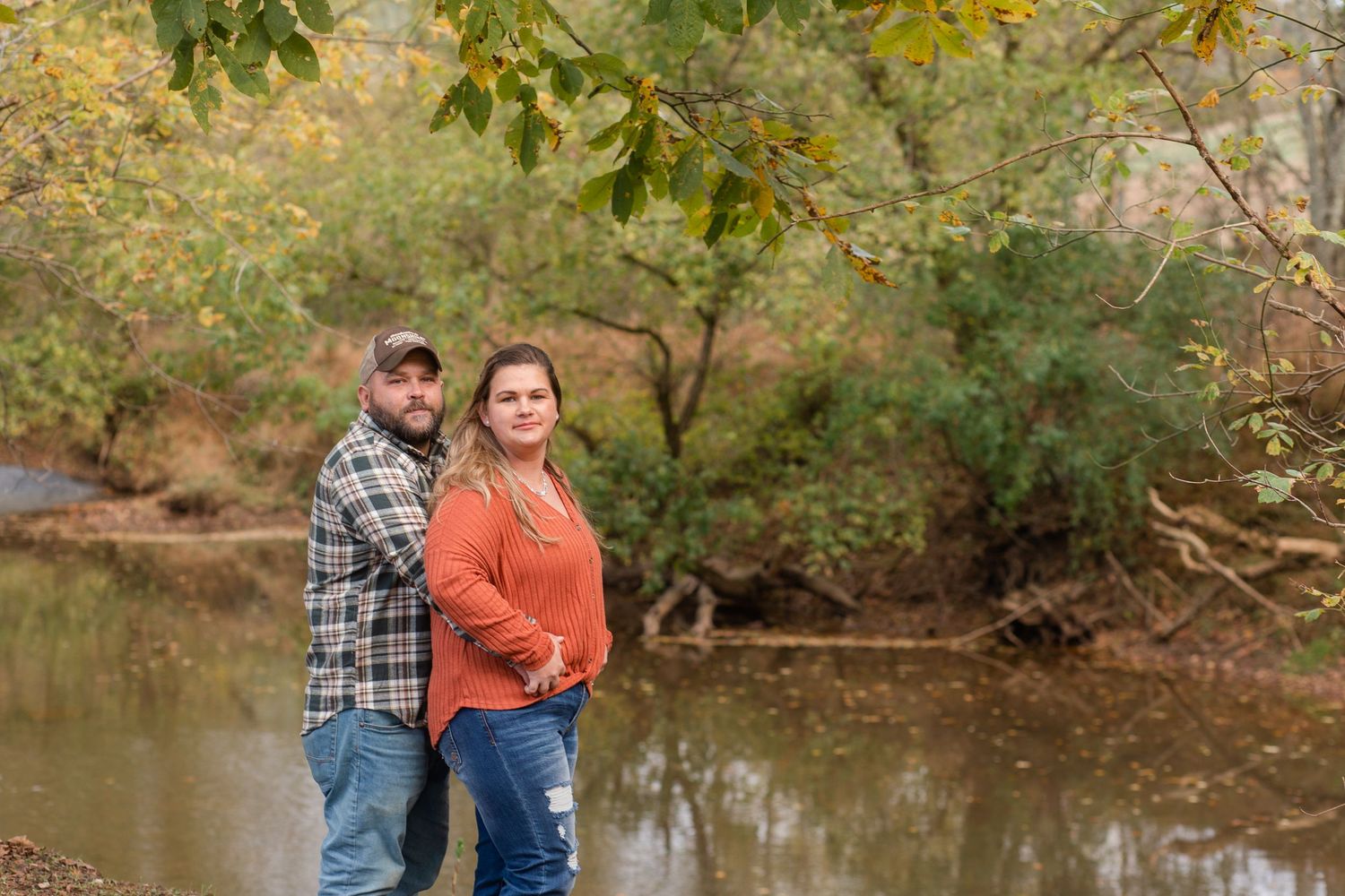 Couple walking together near a serene pond surrounded by autumn foliage.