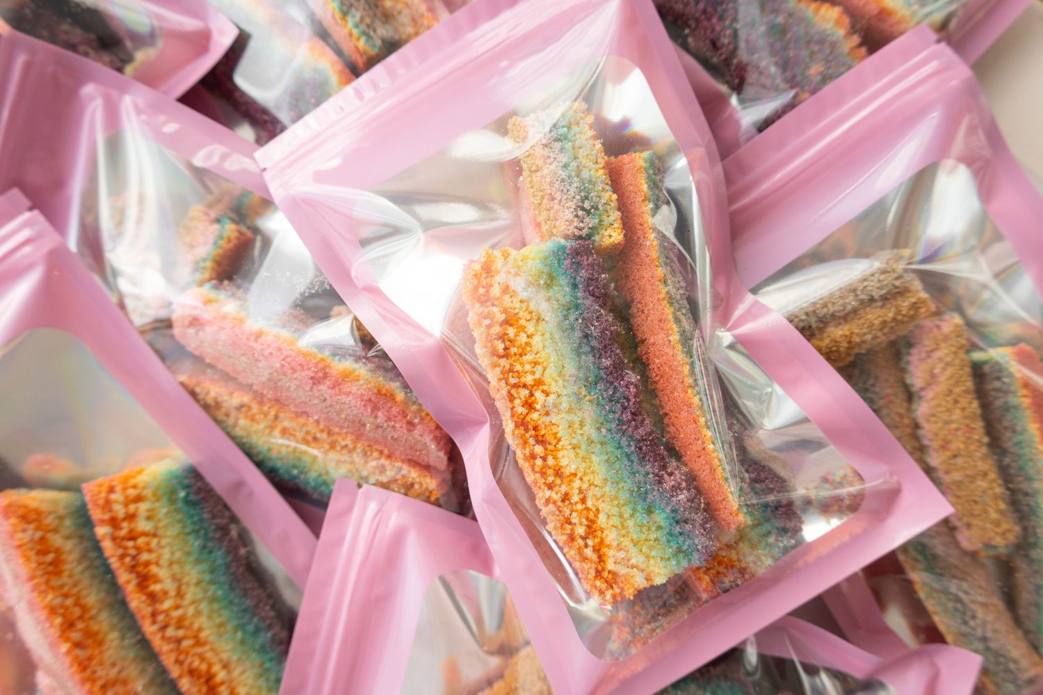 Colorful rainbow sprinkles packaged in small clear plastic bags with pink backgrounds.