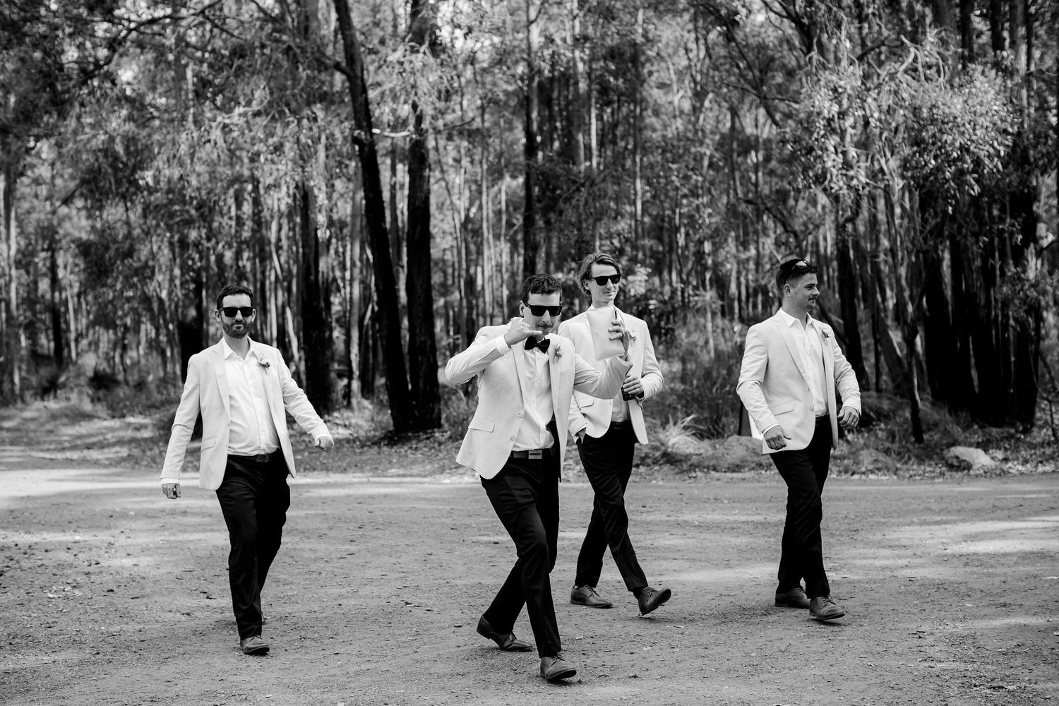 Group of groomsmen walk playfully through wooded area in black and white photography.
