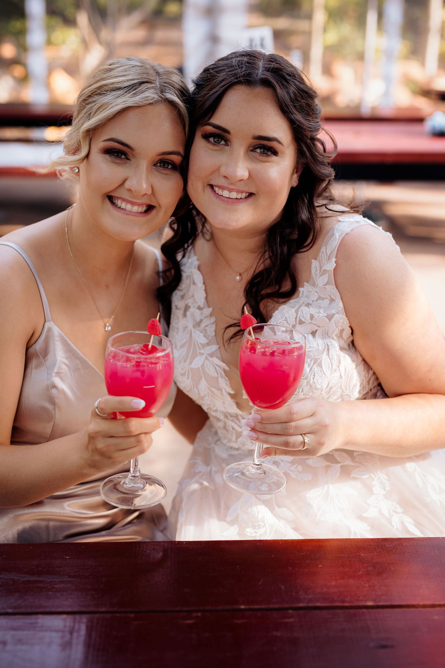 Two friends enjoying bright pink cocktails while dressed in formal attire at outdoor venue.