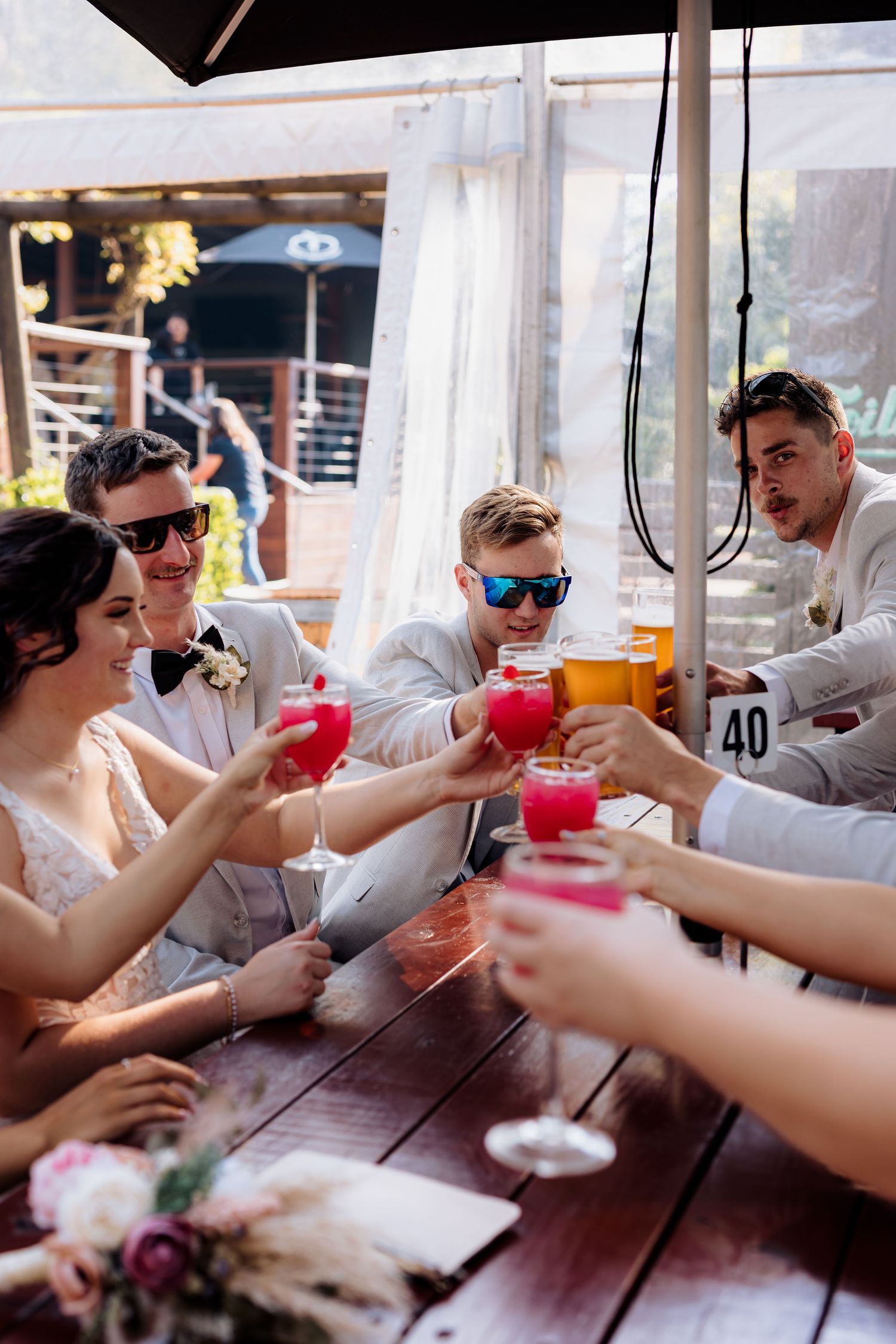 A celebratory toast with red cocktails among wedding guests at an outdoor table.