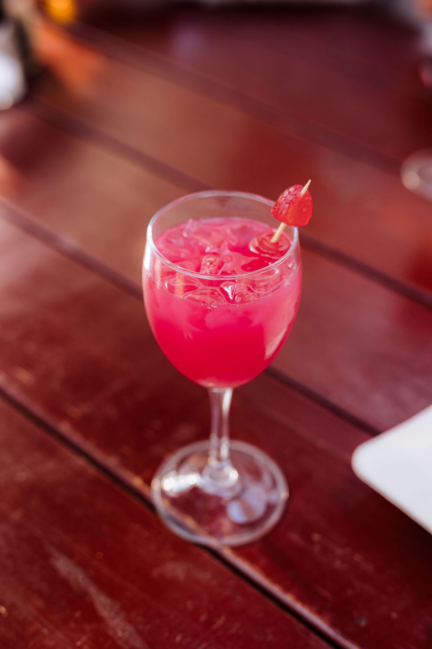 A bright pink cocktail with a garnish served in a stemmed glass on a wooden table.
