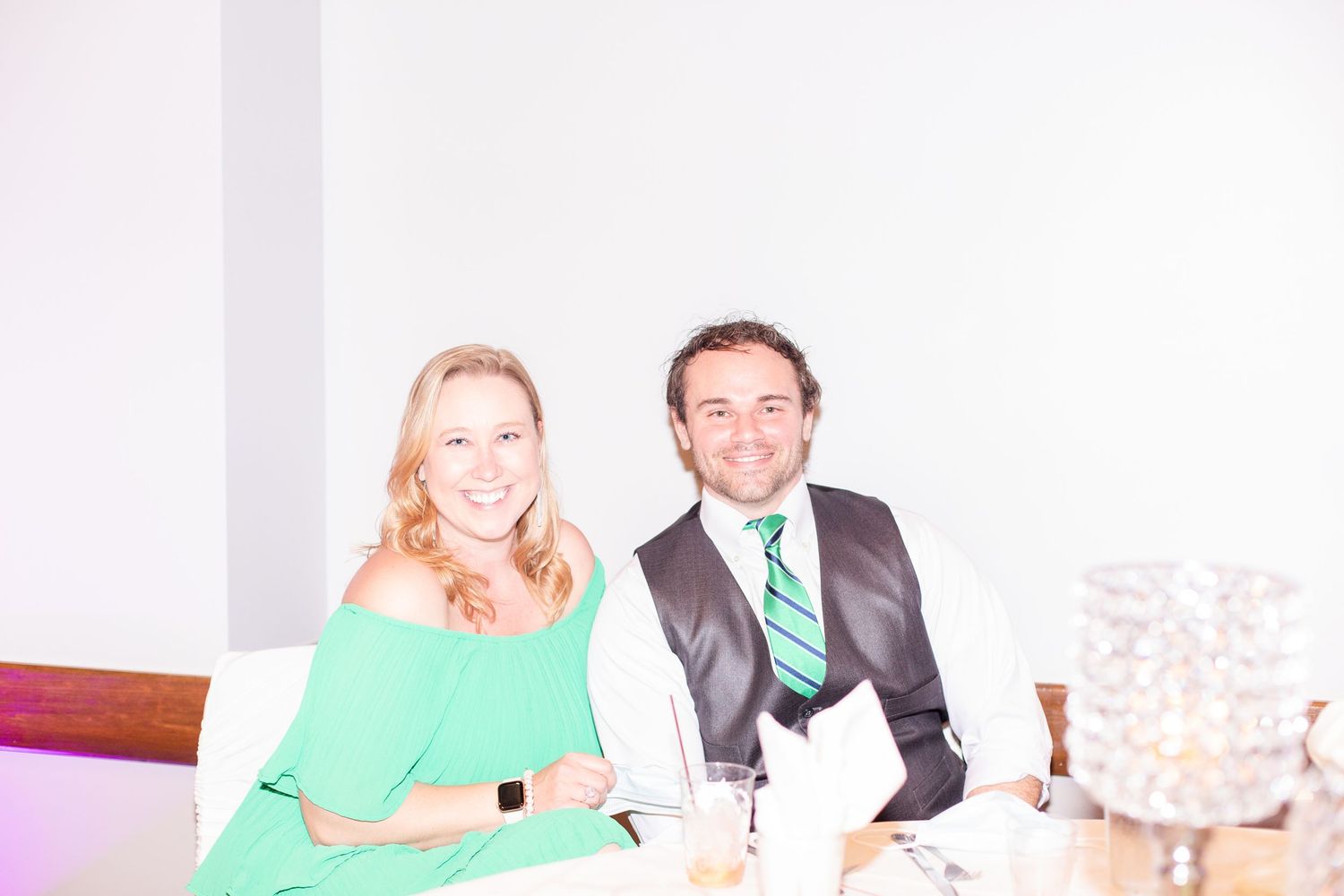 Wedding reception table setting with guests enjoying the celebration in bright lighting.