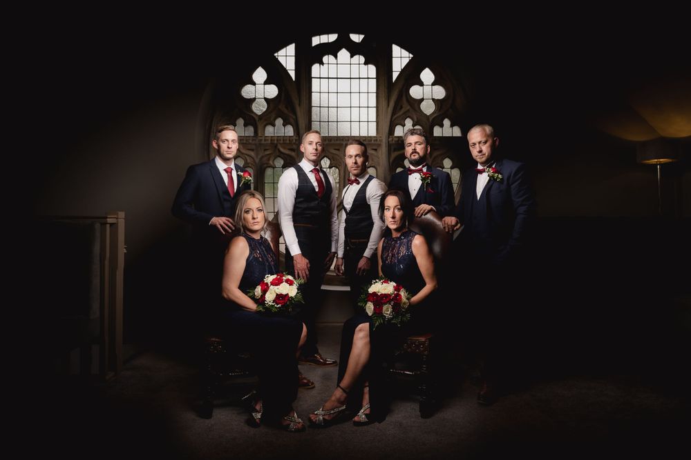 Dramatic wedding party portrait in dark setting with gothic church window backdrop.