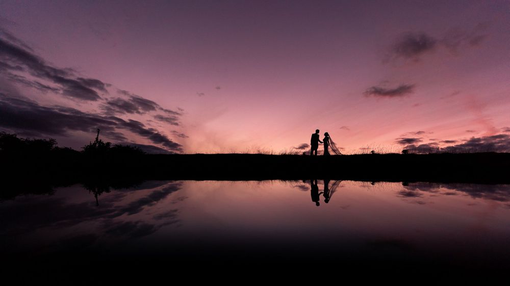 Silhouettes against a vibrant purple sunset sky reflected in calm waters.