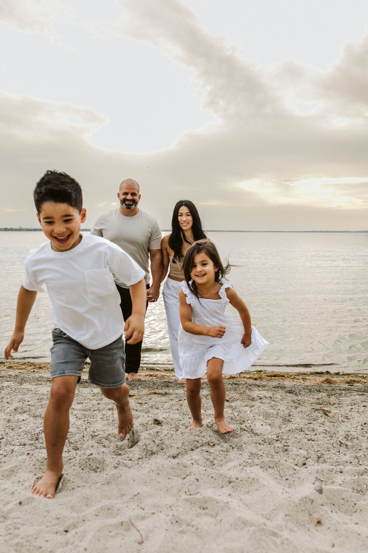 Joyful family playing and running together on sandy beach at sunset.