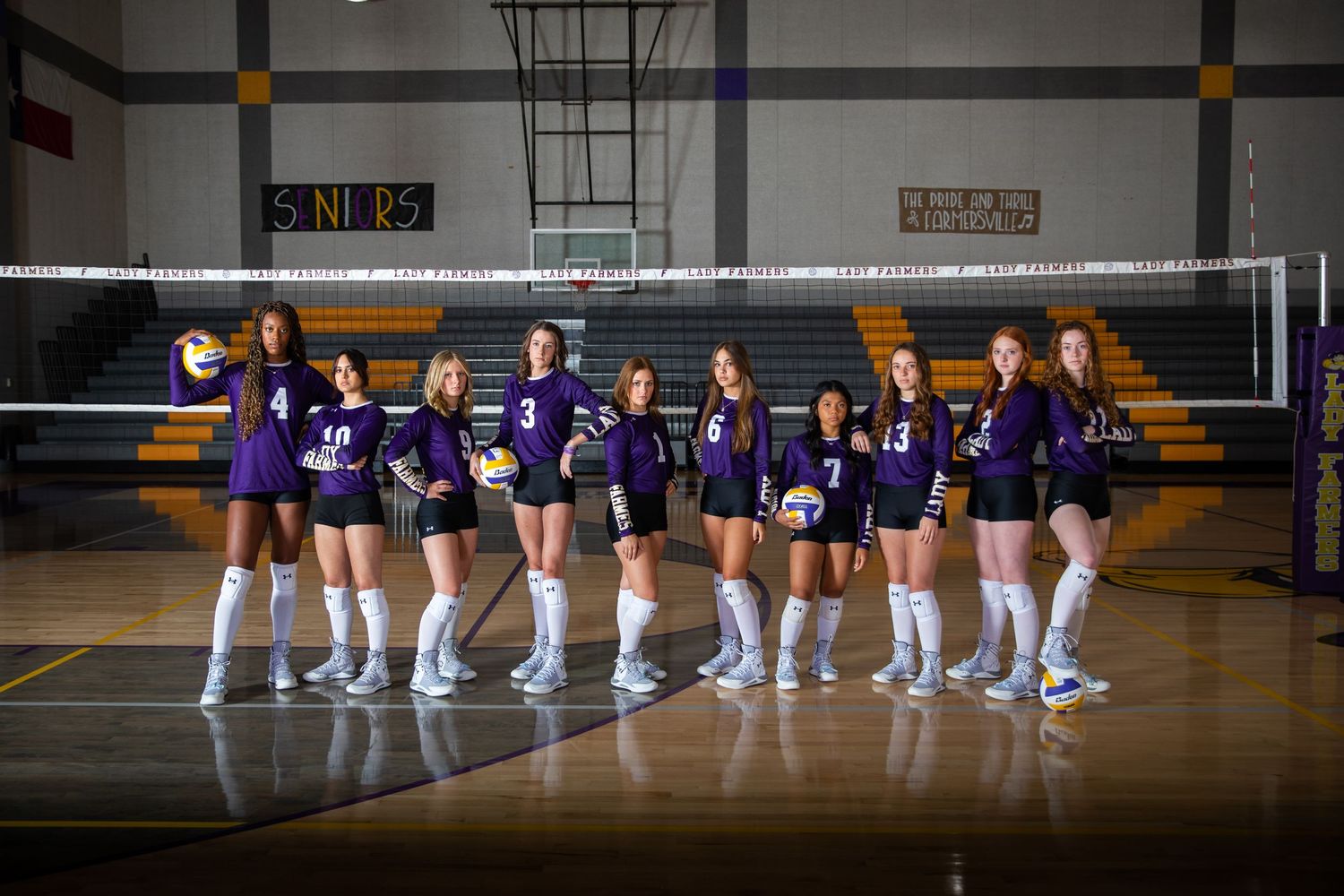 High school volleyball team poses in purple uniforms on court in front of net for team photo.